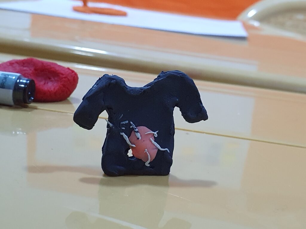 A small clay model of a t-shirt with a heart modelled in the middle with veins coming out.