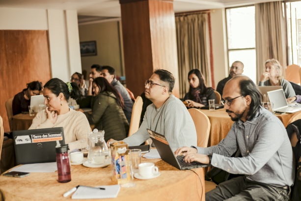 A photo of people in a conference room, sat in circle tables.