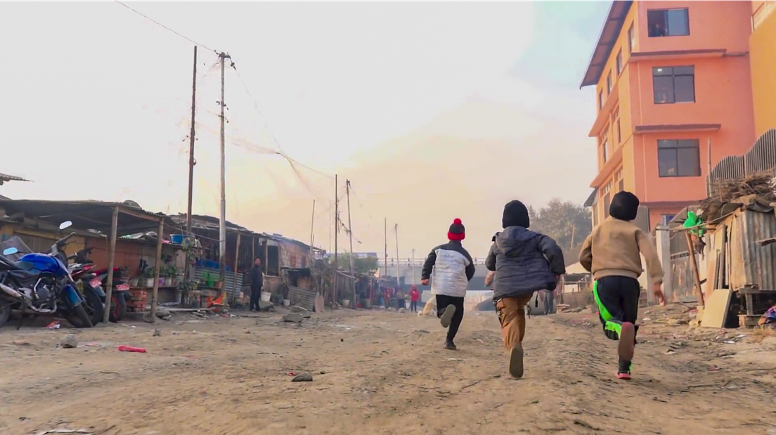 Three children run away from the camera with the sun setting in the background